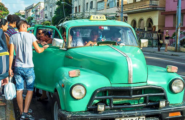 Cubans ride to work in old American car.